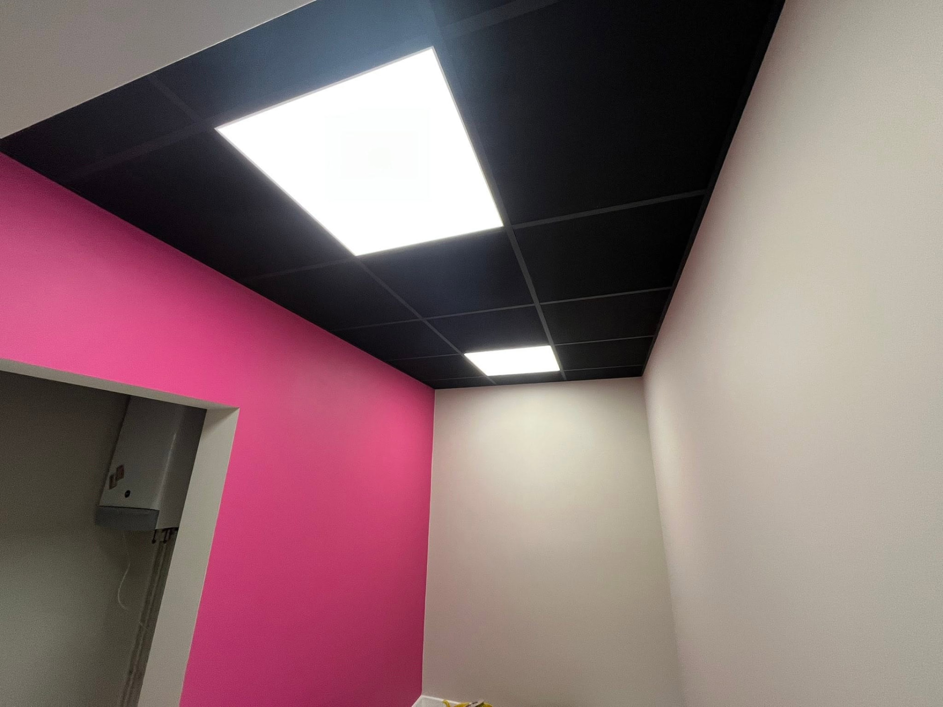 Black suspended ceiling with integrated LED panels and pink feature wall