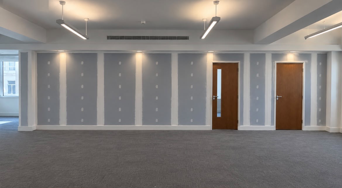 Empty commercial office with newly taped and jointed plasterboard walls, timber doors and suspended ceiling with linear lighting